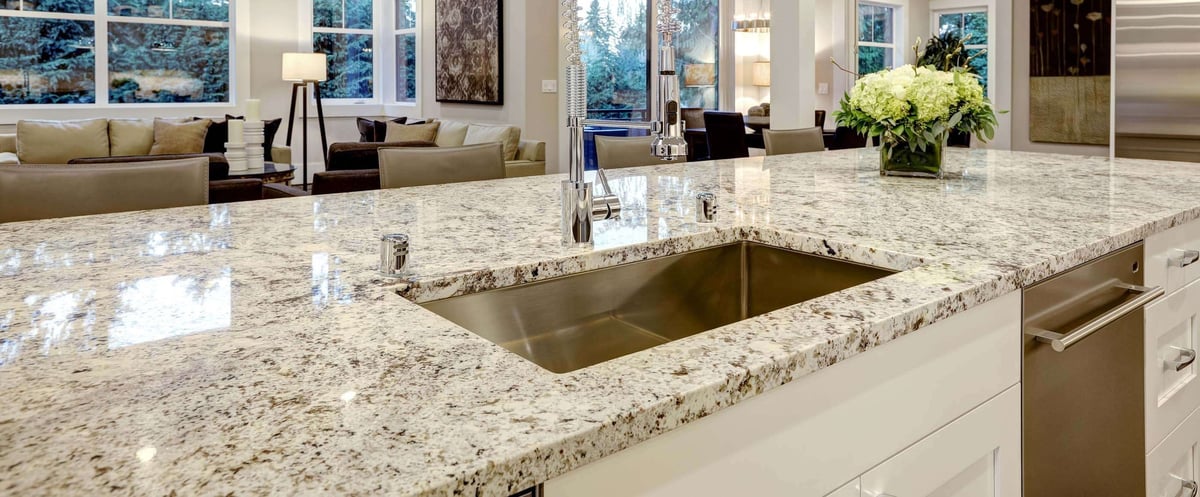Luxury modern kitchen with granite countertops, undermount sink, stainless steel appliances, and living room view in background